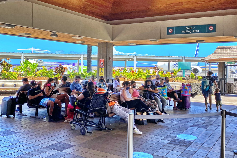 Travelers wearing masks wait at the gate in the open air Kona airport Hawaii
